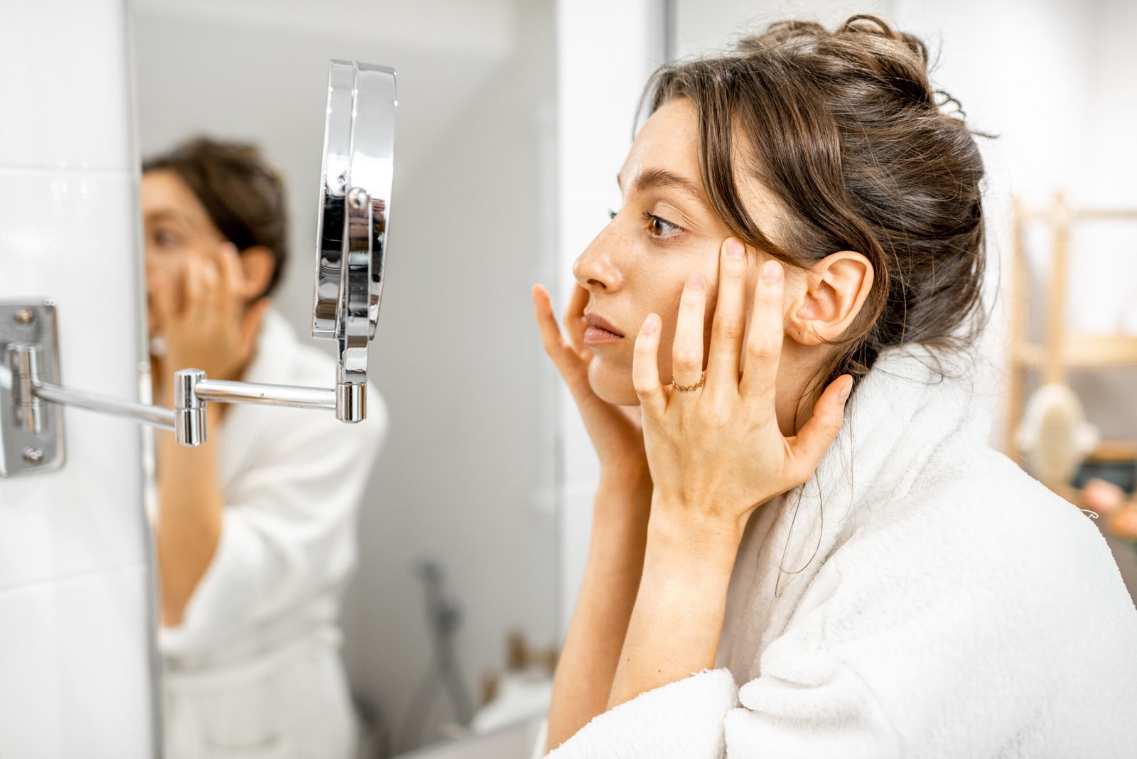 Woman examining her skin in a bathroom mirror at Couture Dermatology